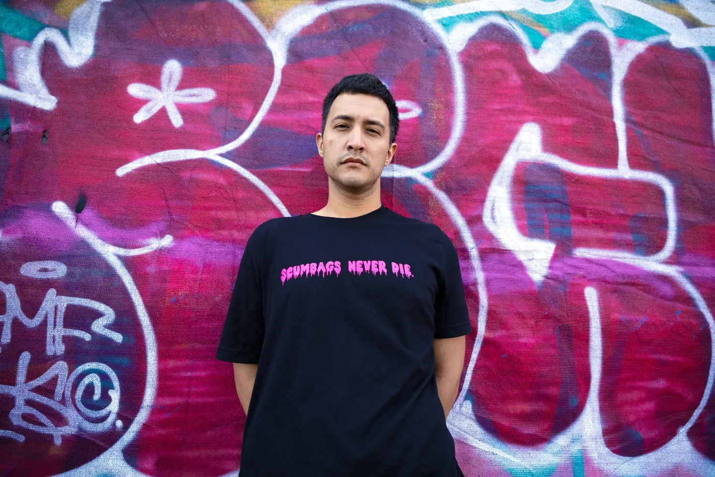 A man standing in front of a wall with graffiti.