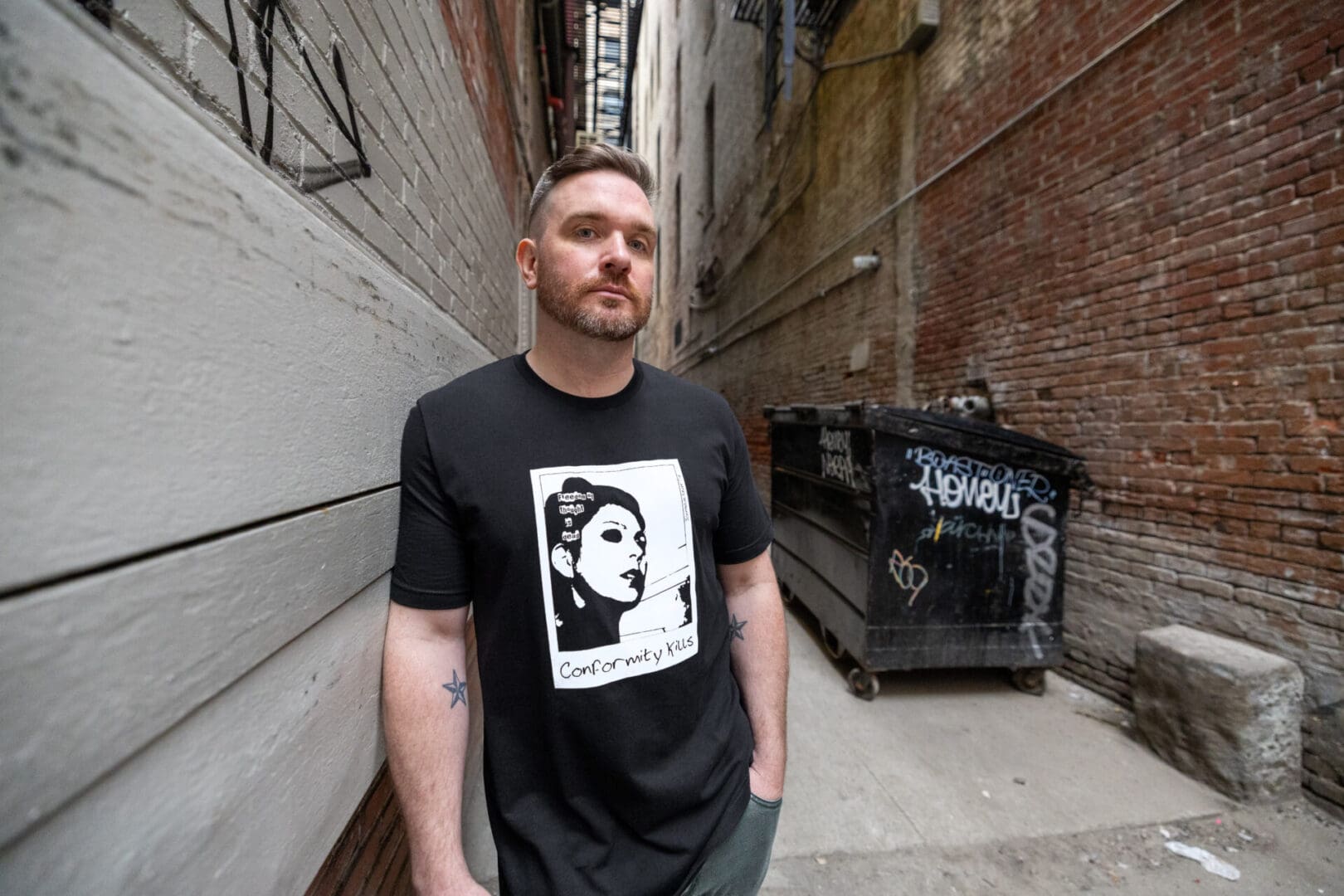 A man standing in an alley way wearing a black shirt.